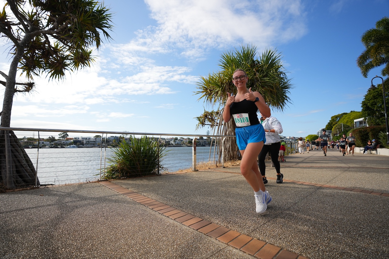 A Run2Cure participant giving two thumbs up while running the riverside path at New Farm