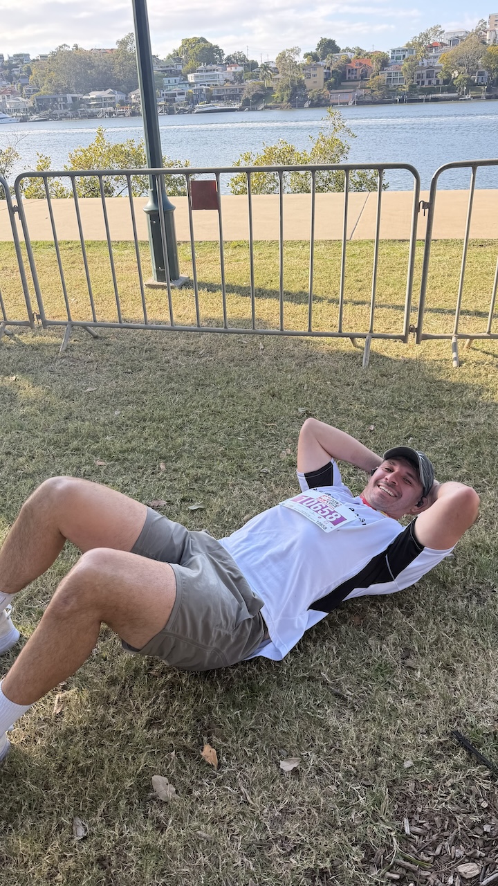 A Run2Cure runner stretched out on the grass at New Farm Park after finishing
